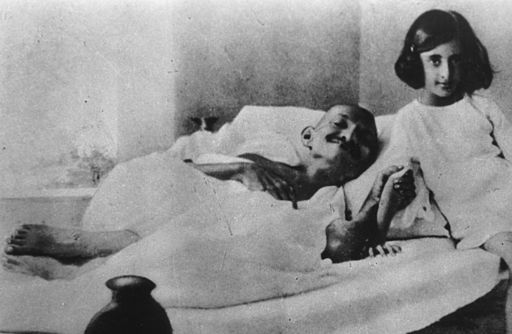 Photograph of Gandhi in bed, holding arm of Indira, sitting beside him)