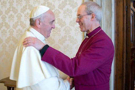 Anglican News photo.  Smiling Pope Francis and Archbiship of Canterbury Welby greet each other, shaking hands and hand on shoulder.