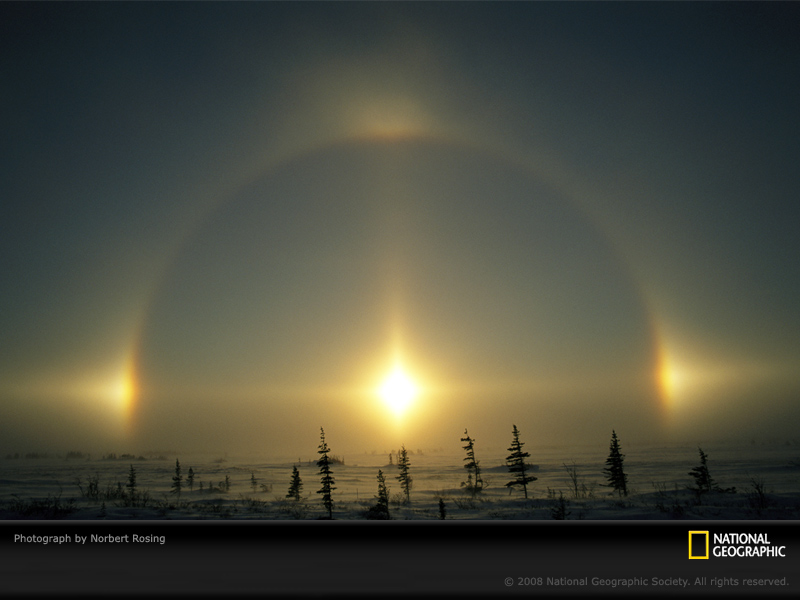 A photograph of the sun surrounded by a large circle of light, with four bright lights at the top, bottom, and sides, connected by a cross of light.